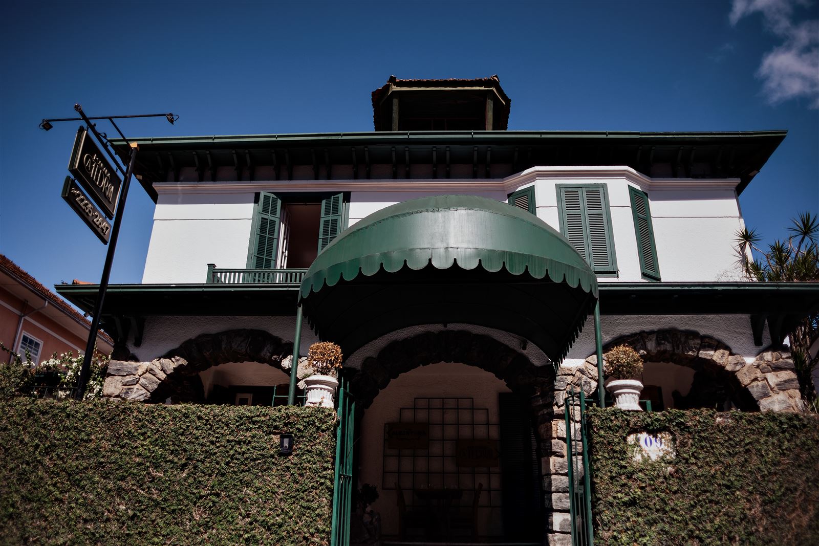 Entrada da pousada com arcos de pedra e toldo verde